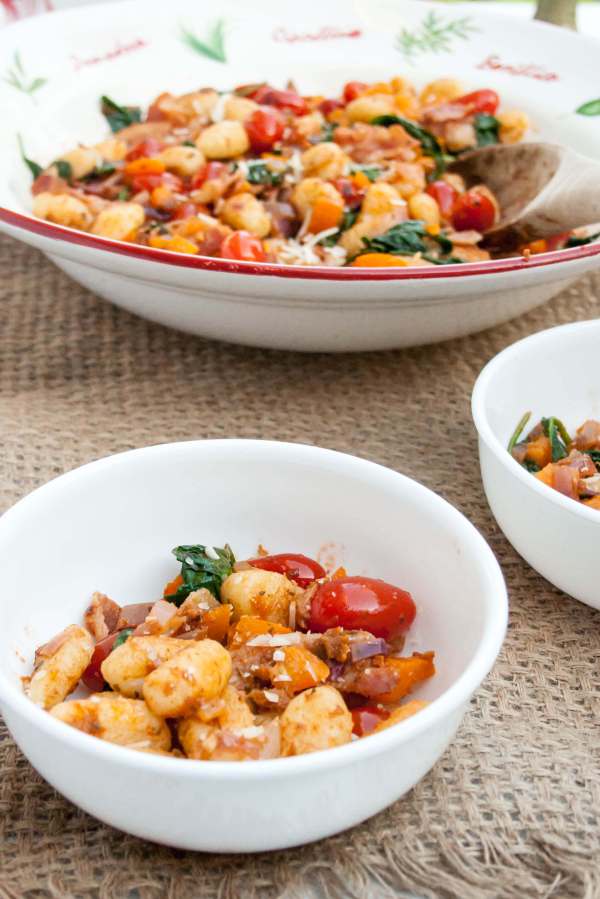 Gnocchi fried in a skillet with cherry tomatoes, bacon, spinach, yellow peppers and pesto. What a great weeknight meal!